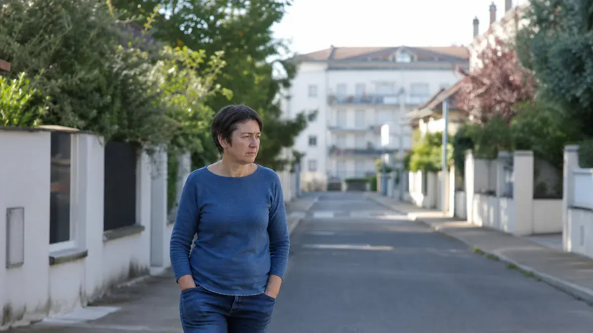 Femme en pull bleu marchant seule, les mains dans les poches, dans une rue résidentielle déserte